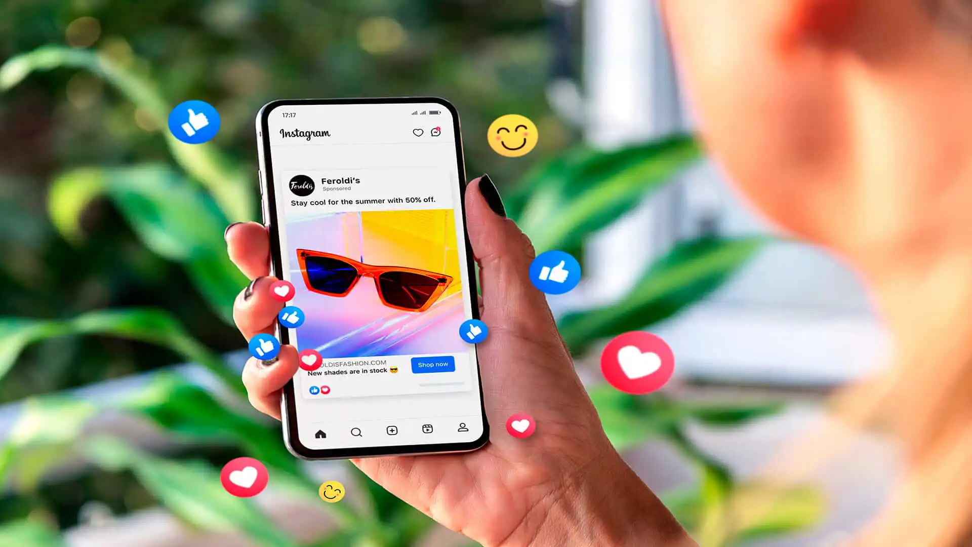 Hånd holder en smartphone med en Instagram-annonce for solbriller, omgivet af reaktionsemojis.