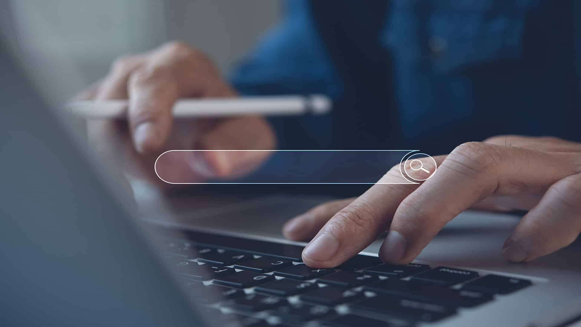 Hånd, der bruger en bærbar computer med en søgefelt over skærmen.